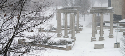 Snow-covered colonnade and trees in a wintry scene.