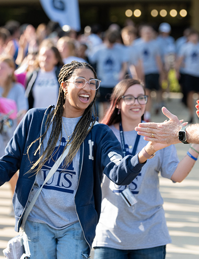 Two students smile while slapping the extended hands of faculty and staff at Convocation.