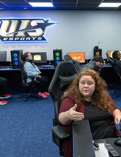 An instructor speaks to students sitting in gaming chairs in the Esports Arena.