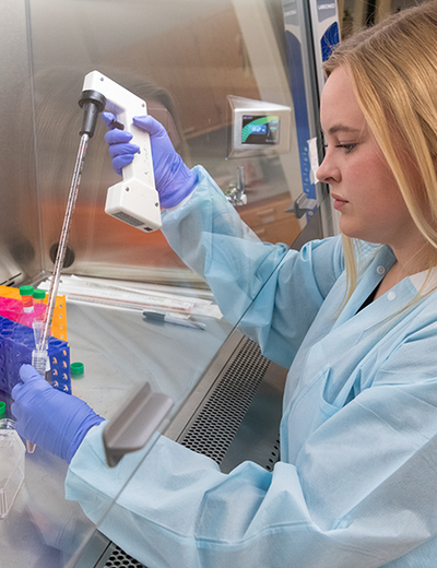 Student in a lab coat and gloves using a pipette for research in a sterile lab environment.