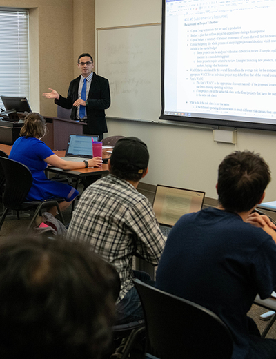 Students sitting at desks in a classroom as a professor teaches. 