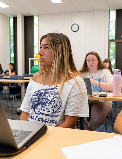 Students attentively listen in a classroom, taking notes and using laptops during a lecture at the University of Illinois Springfield.