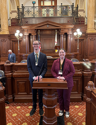 Two students pose on the floor of the Illinois State Senate.