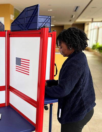 Student casts ballot at a red, white and blue voting booth inside the University of Illinois Springfield student union.