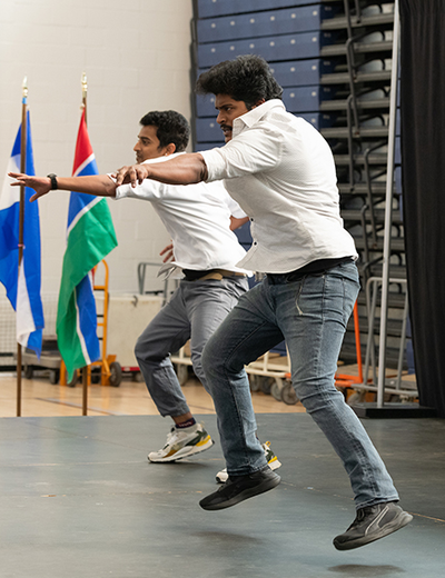 Two people in white shirts and jeans perform a synchronized dance on stage during a cultural event.