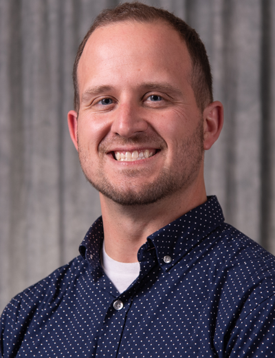Smiling man in a dark shirt against a gray curtain backdrop, portrait photograph.