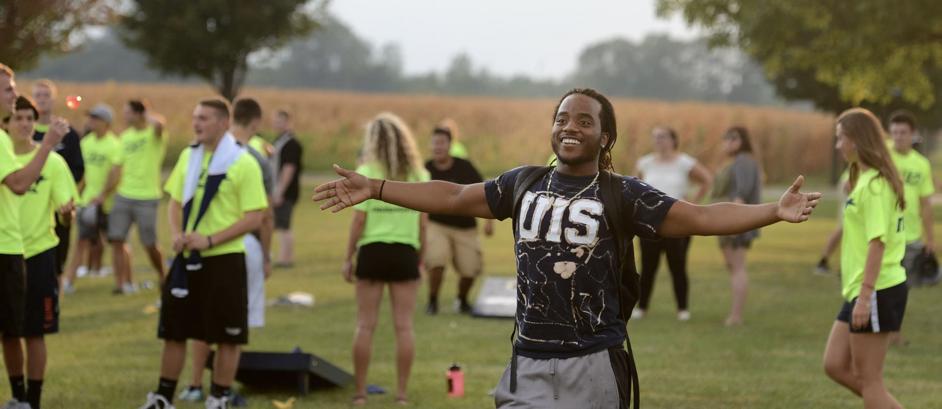 student standing in a field with his arms open