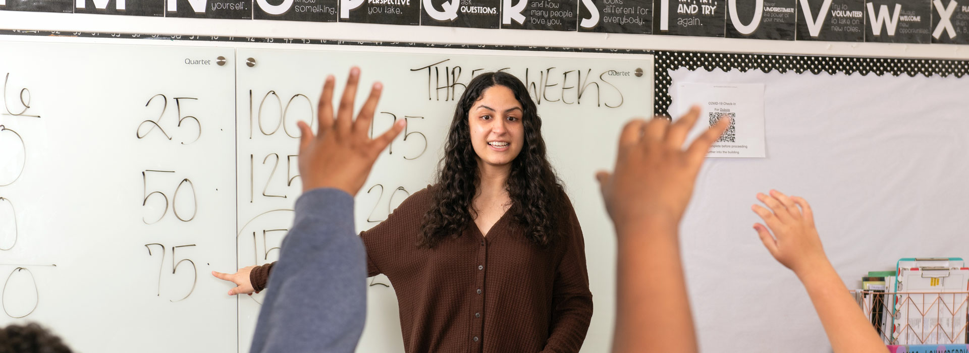 a teacher in the middle of a classroom with lots of raised hands