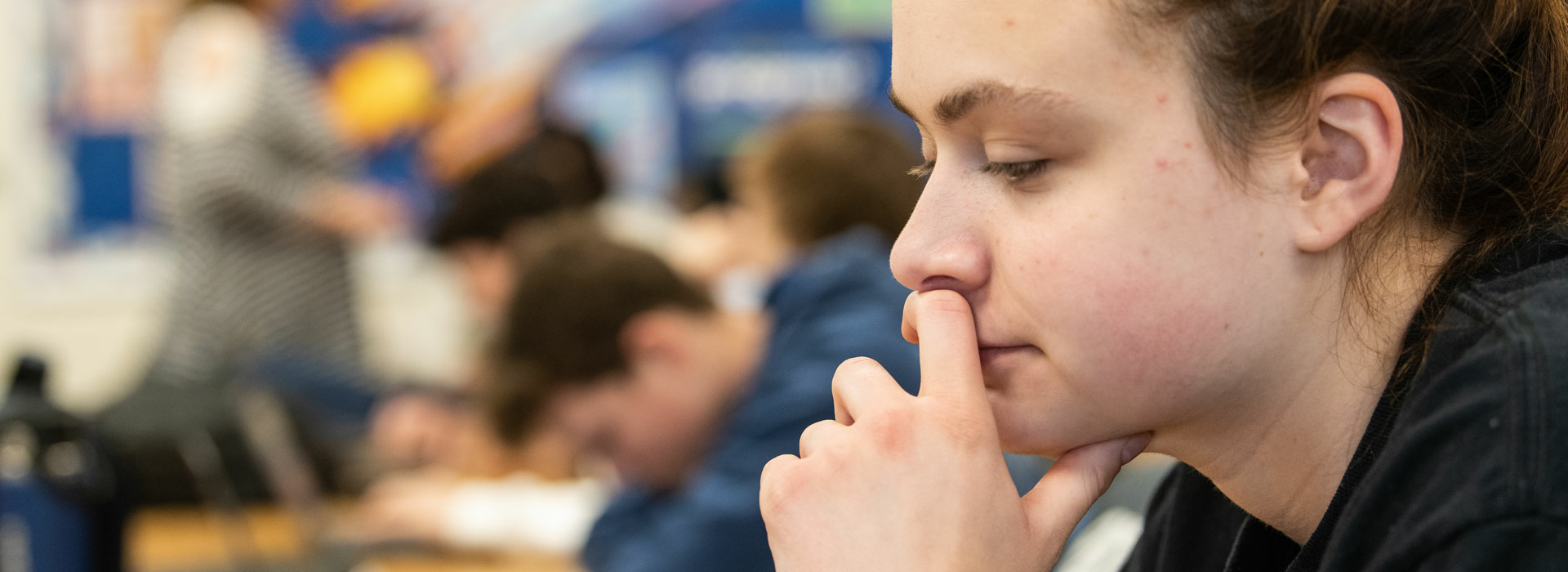 a student at their desk in a classroom looking down at a laptop