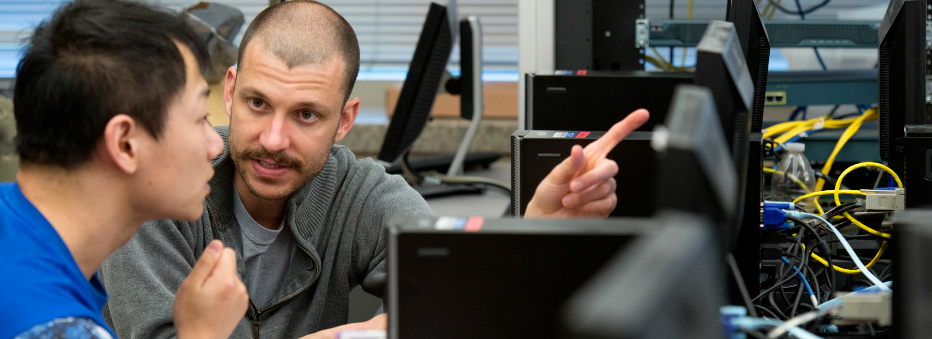 a professor showing a student something on a computer while they sit at a desk