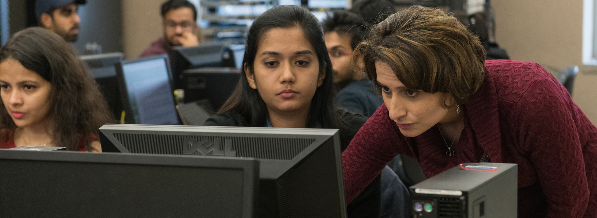 a professor standing next to a student at a computer desk showing the student something on a computer