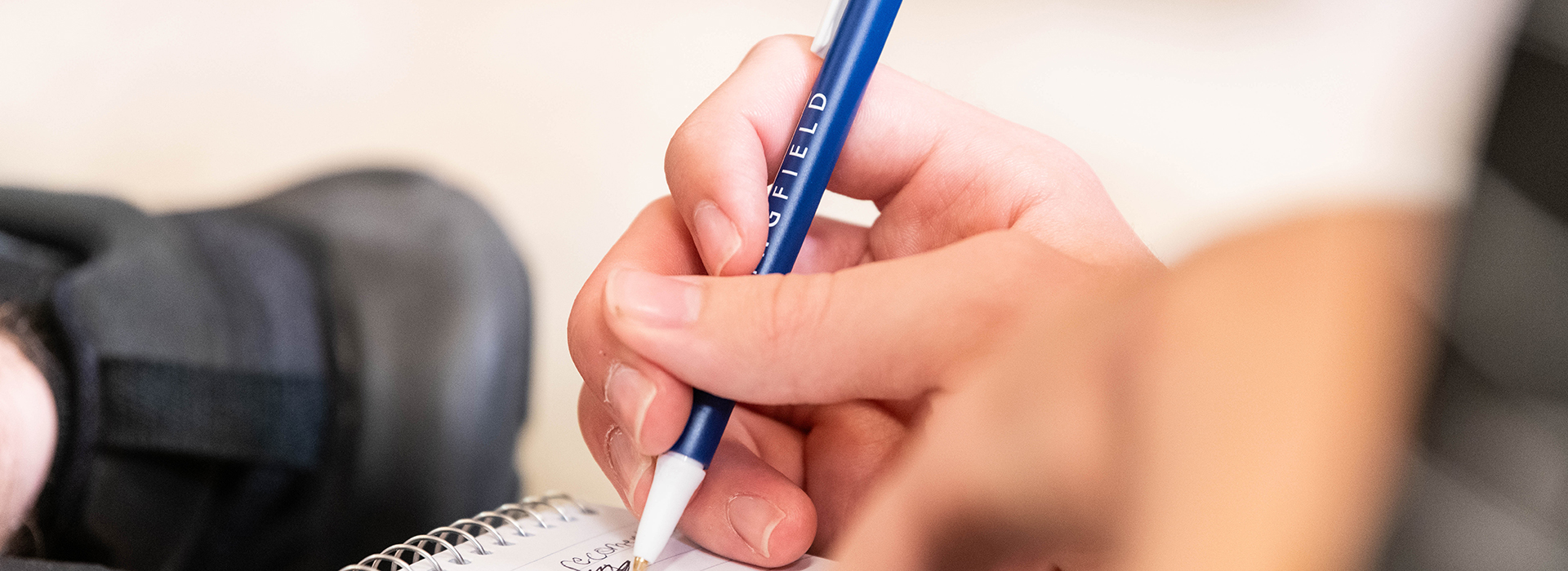 closeup image of a hand writing with a blue UIS pen